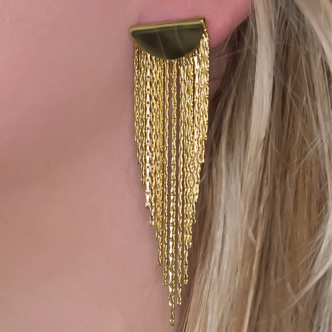 Close-up van de Golden Fringe oorbellen, met een gouden plaatje en lange franjes in verschillende lengtes die in een punt lopen, gemaakt van stainless steel, waterproof, hypoallergeen en verkleuren niet.